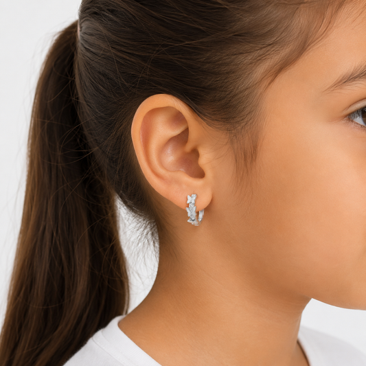 Niña de 6 años usando argollas de plata ley 925 con mariposas y brillos, mostrando cómo el diámetro de 11mm queda ceñido y cómodo en el lóbulo de la oreja.
