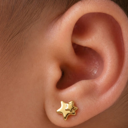 Primer plano de la oreja de una bebé recién nacida usando un aro abridor de estrella doble de oro macizo de 18k. El aro de 4 mm es proporcional a la oreja de la bebé, y el tope a presión asegura comodidad y seguridad.