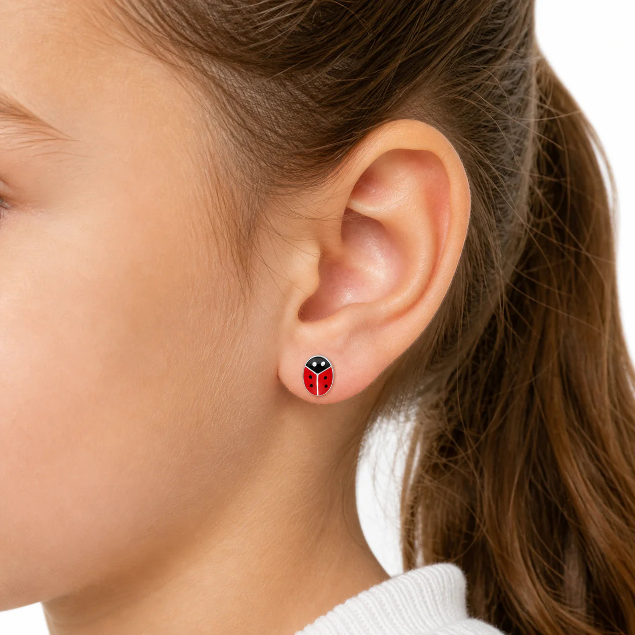 Primer plano de la oreja de una niña usando un aro de plata 925 con diseño de chinita esmaltada. El aro de 8x5mm destaca por sus colores brillantes y su ajuste seguro y proporcional para niñas mayores de 6 años.