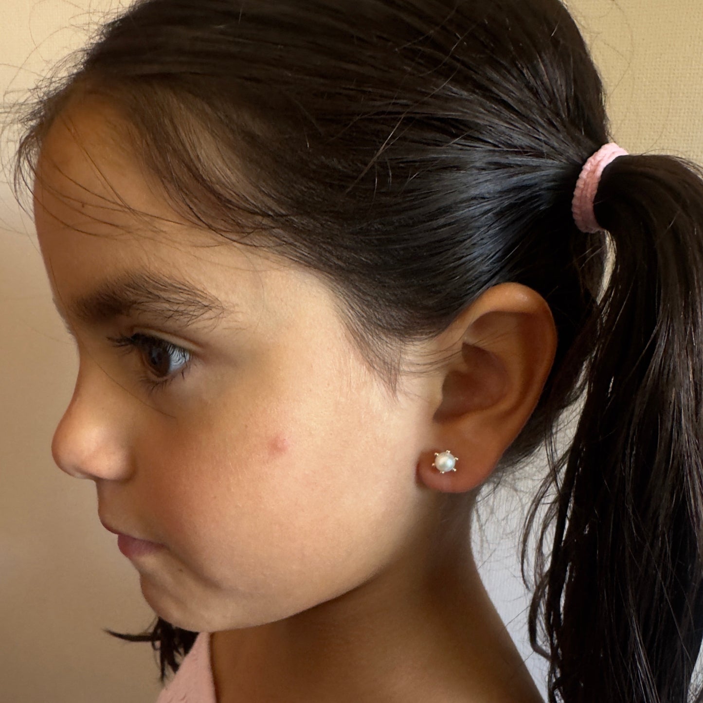 "Niña de 6 años luciendo aros de oro 18k modelo pistilo con perla cultivada, destacando el tamaño proporcional de 7mm y el ajuste seguro y cómodo en la oreja."