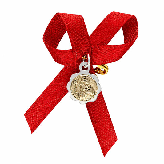 Medalla bicolor de San Benito Abad en plata ley 925 con lazo de cinta roja satinada y alfiler de gancho dorado para recién nacido sobre fondo blanco.