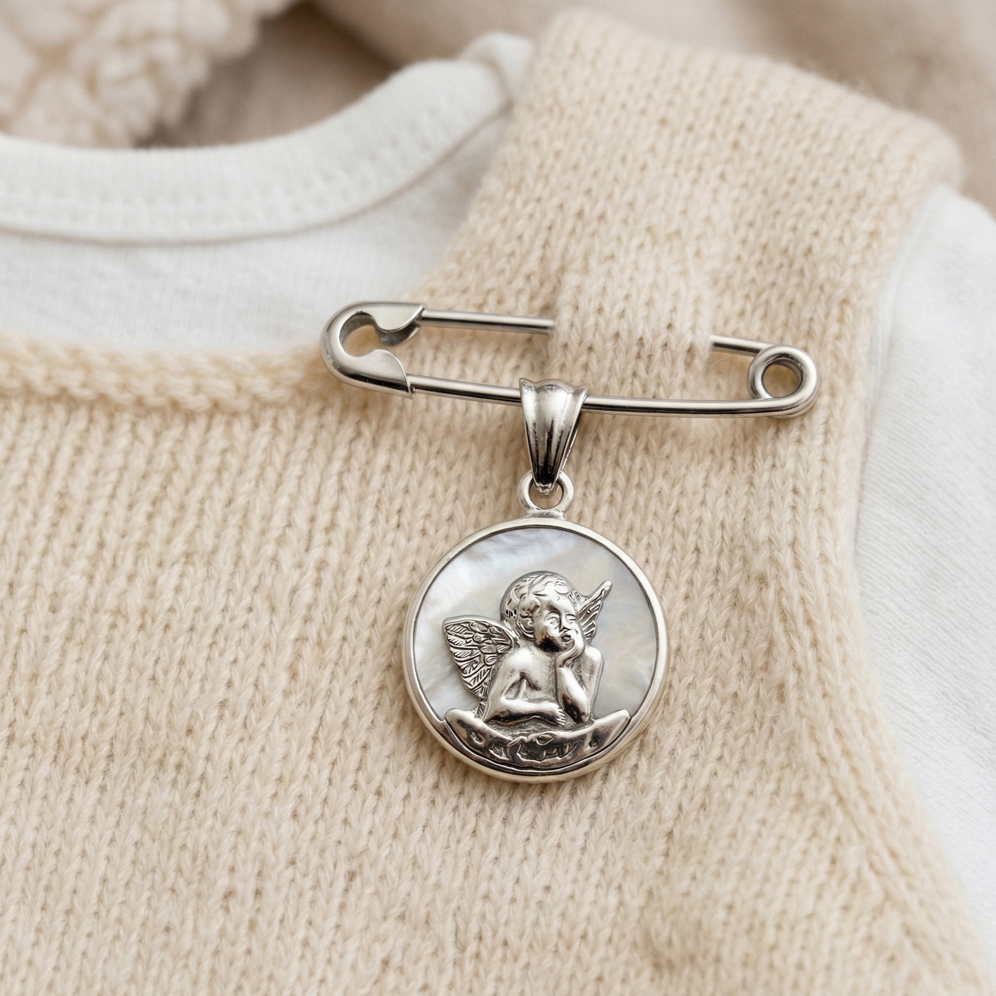 alfiler de gancho de plata con medalla angel de la guarda puesto en la ropita de un bebe