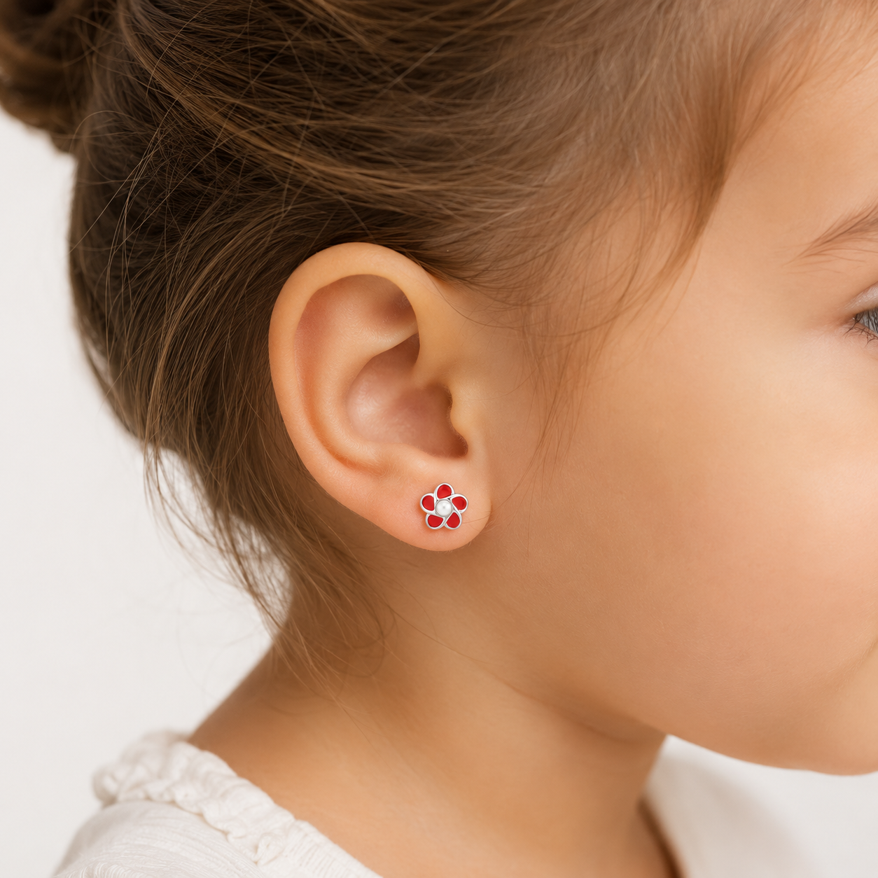 Primer plano de una niña de tres años luciendo un aro de plata ley 925 con forma de flor roja y perla central, mostrando cómo el tamaño de 7mm se ajusta delicadamente a su oreja.