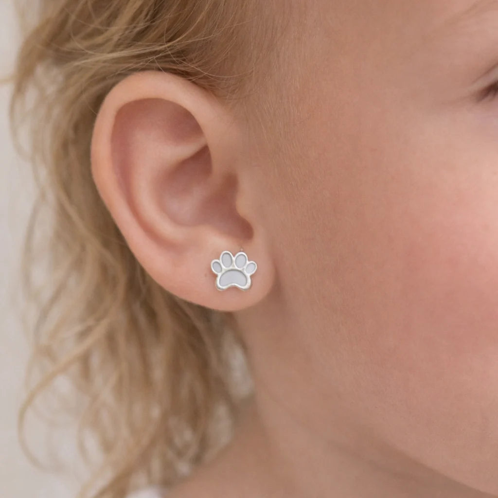"Detalle de una niña de 3 años luciendo un tierno aro de plata 925 con diseño de patita blanca esmaltada que destaca con un brillo sutil en su oreja."